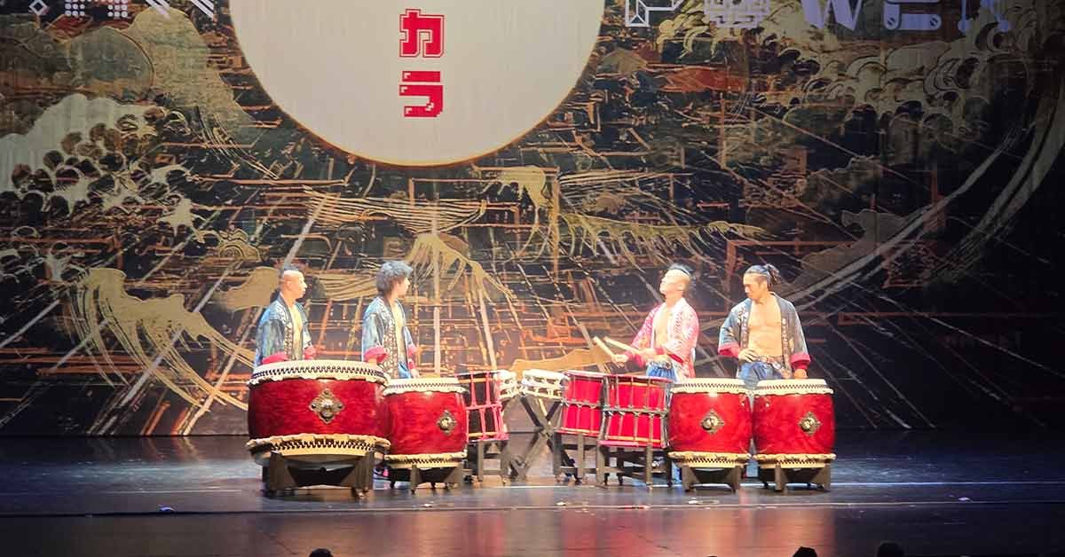 Four Yamato drummers performing on stage in Basel, standing behind large red taiko drums with traditional Japanese patterns in the background.