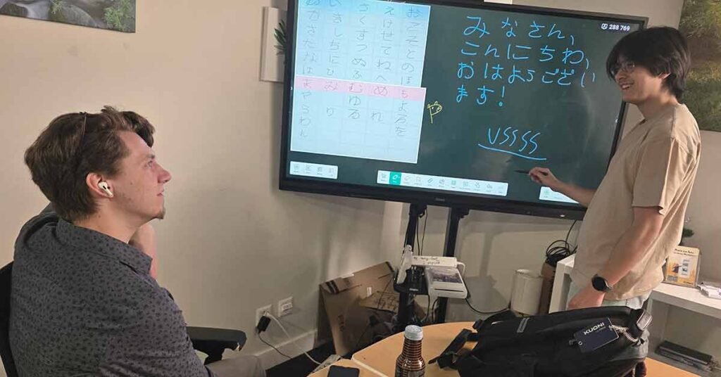 Two students practicing Japanese writing and speaking together in class using an interactive screen.